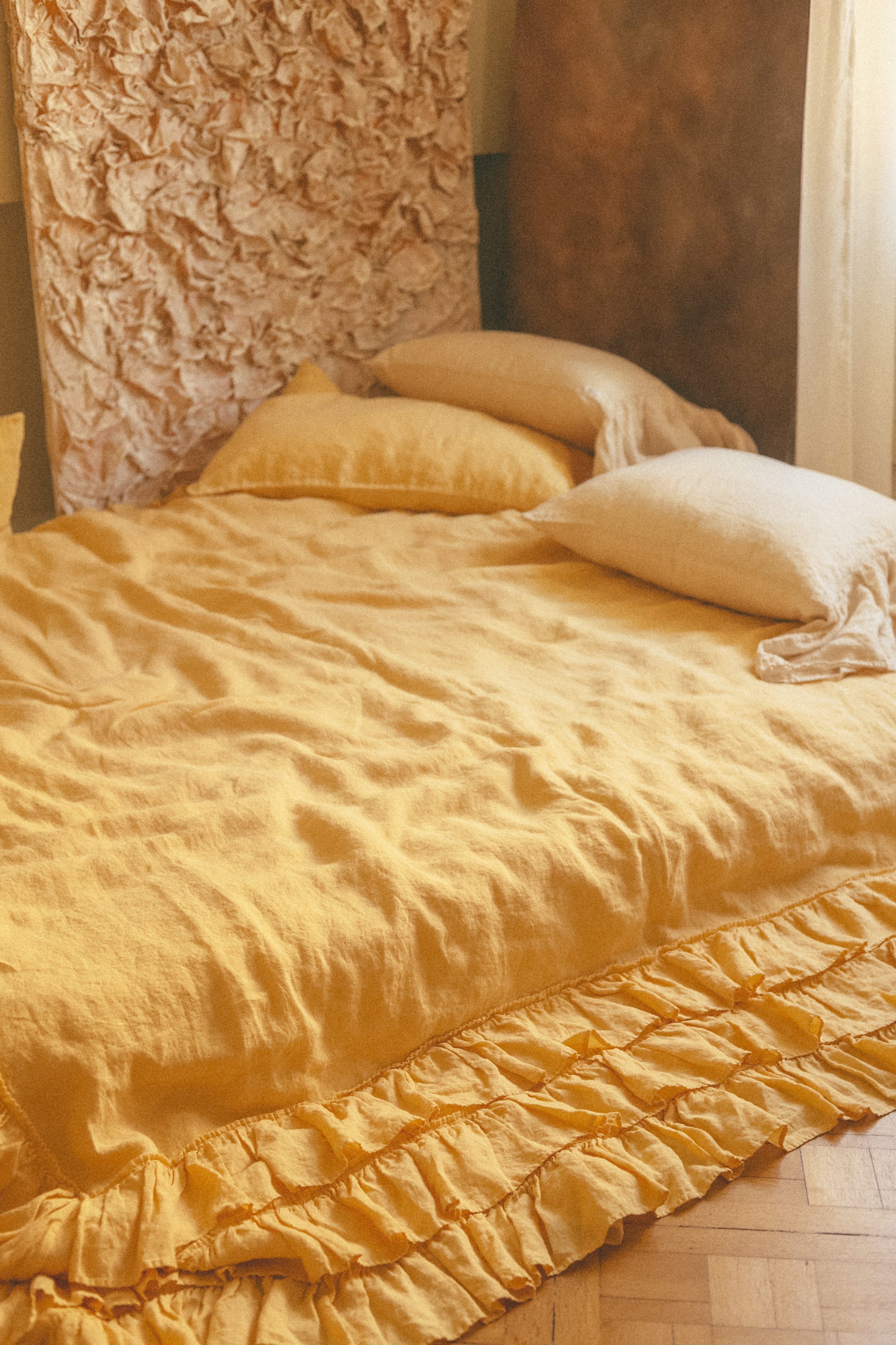 Yellow bedding with ruffled edges on a bed against a textured wall.